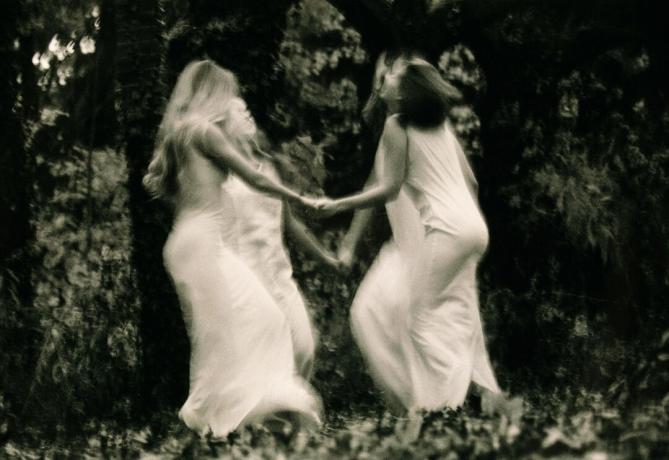 Neli noort naist, kes tantsivad metsas, kätest kinni (mustvalge, hägune liikumine)