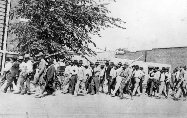 Rühm rahvuskaardi vägesid, kes kannavad tääkidega vintpüssi, eskortivad relvastamata mustanahalisi mehi kinnipidamiskeskusesse pärast Tulsa rassi veresauna, Tulsa, Oklahoma, juuni 1921.